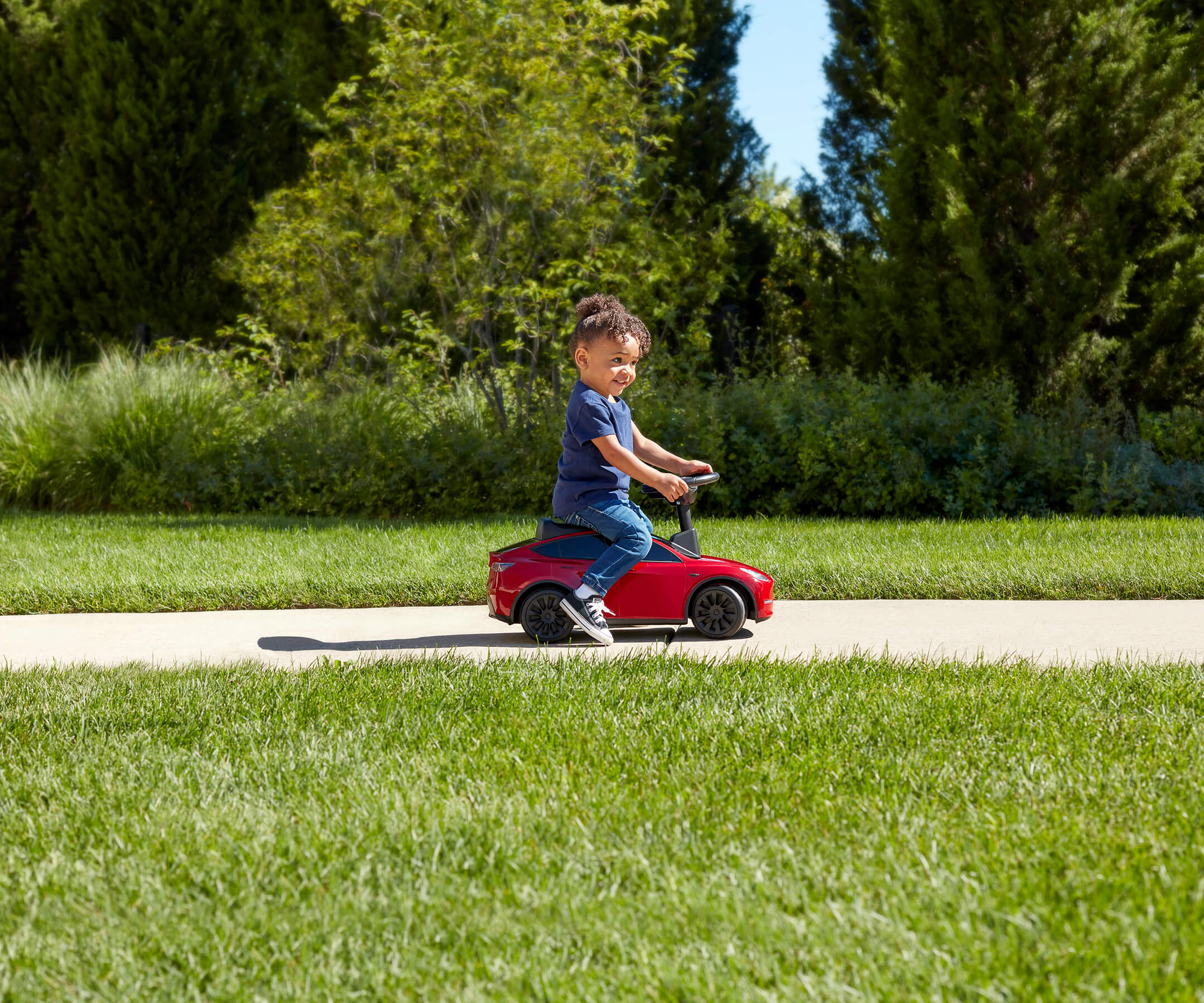Child riding red Tesla Model Y for kids down the sidewalk