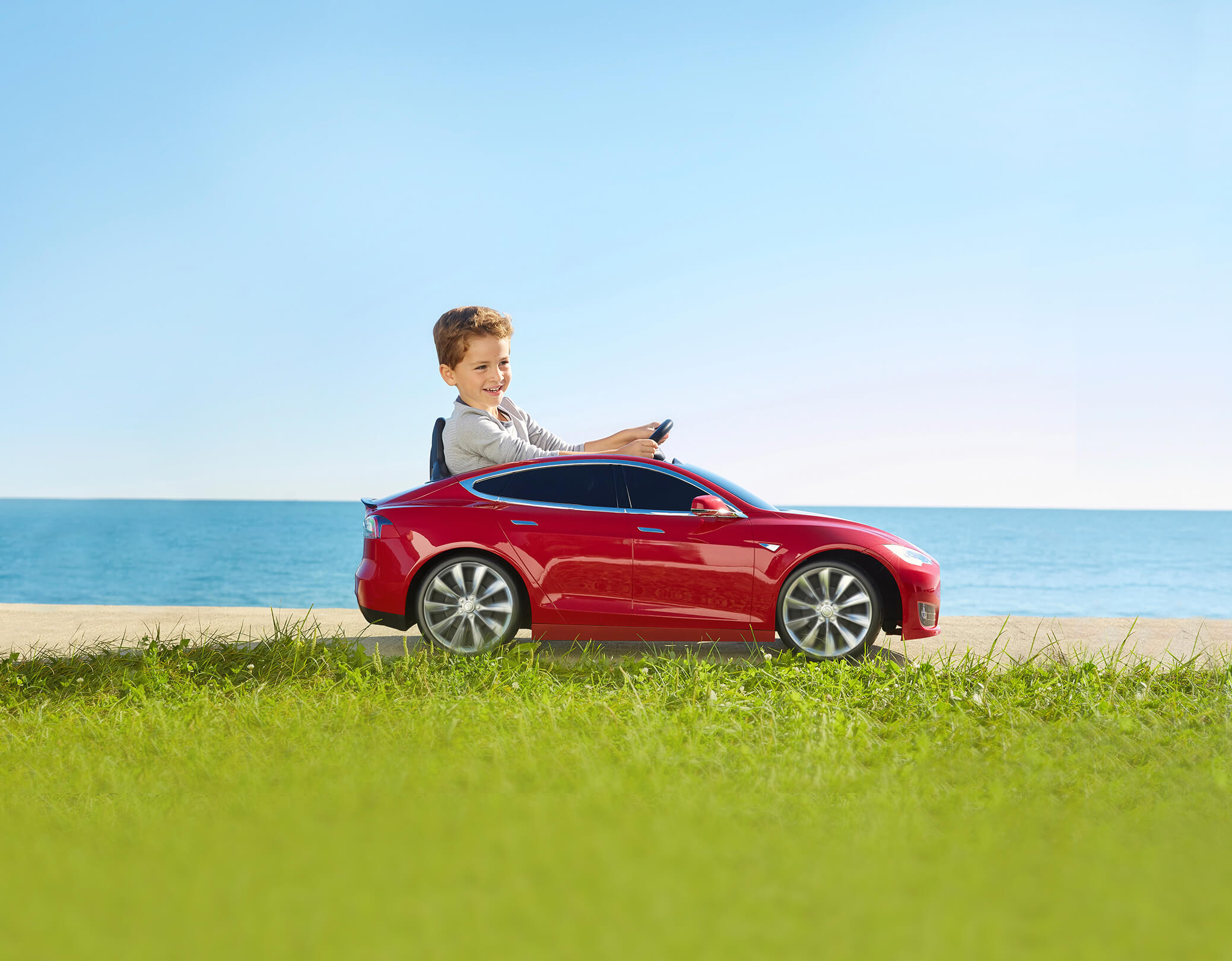 Child riding red Tesla Model S for kids down the sidewalk